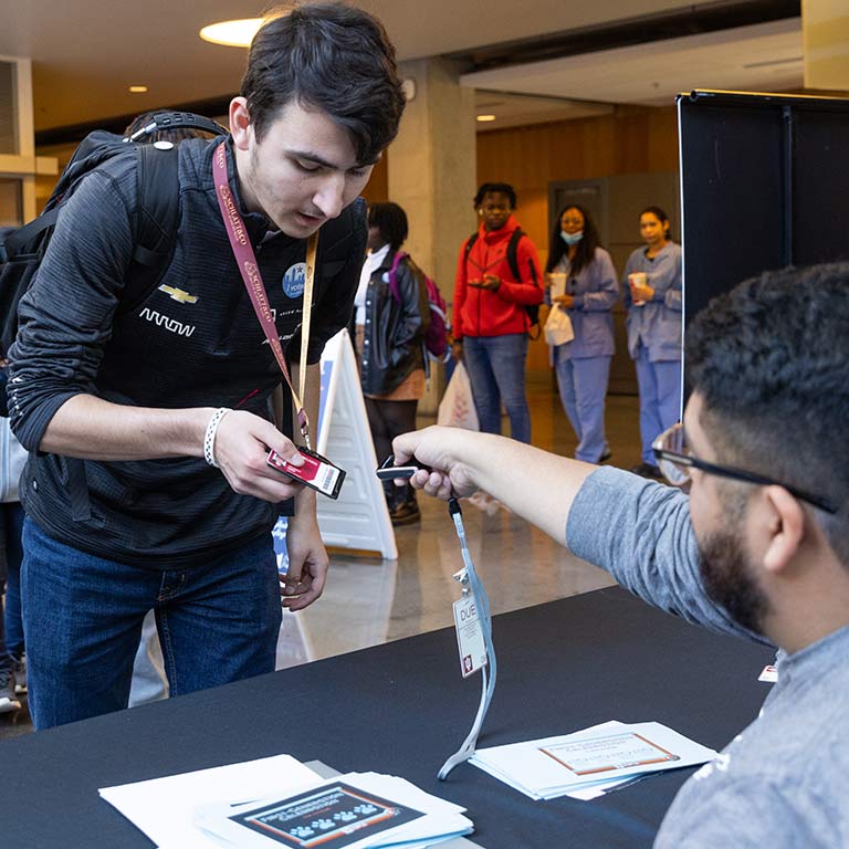 An event attendee leans over a table for a staff member to scan a barcode on his nametag