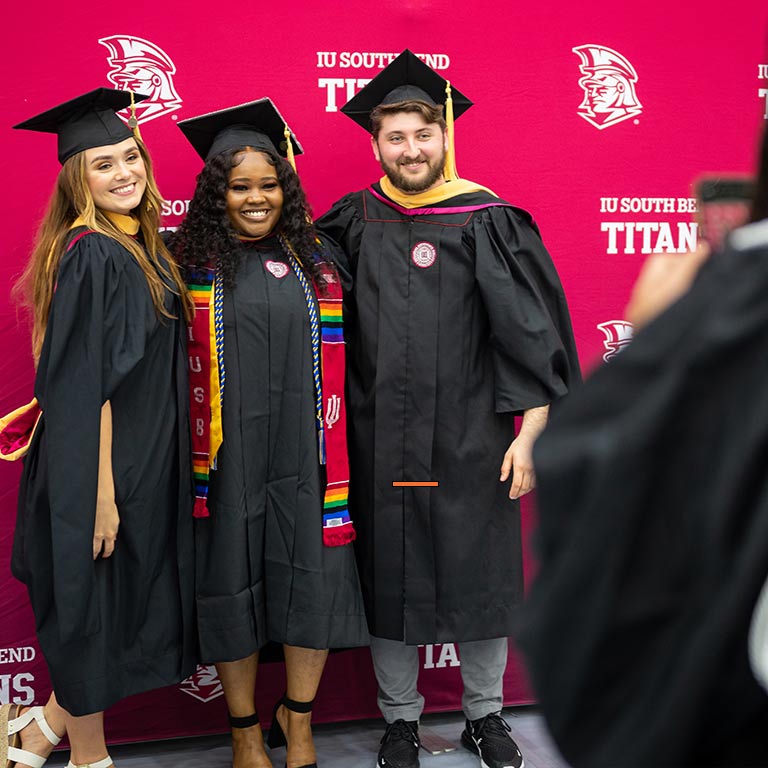Three IU South Bend graduates pose in front of a backdrop for a photo
