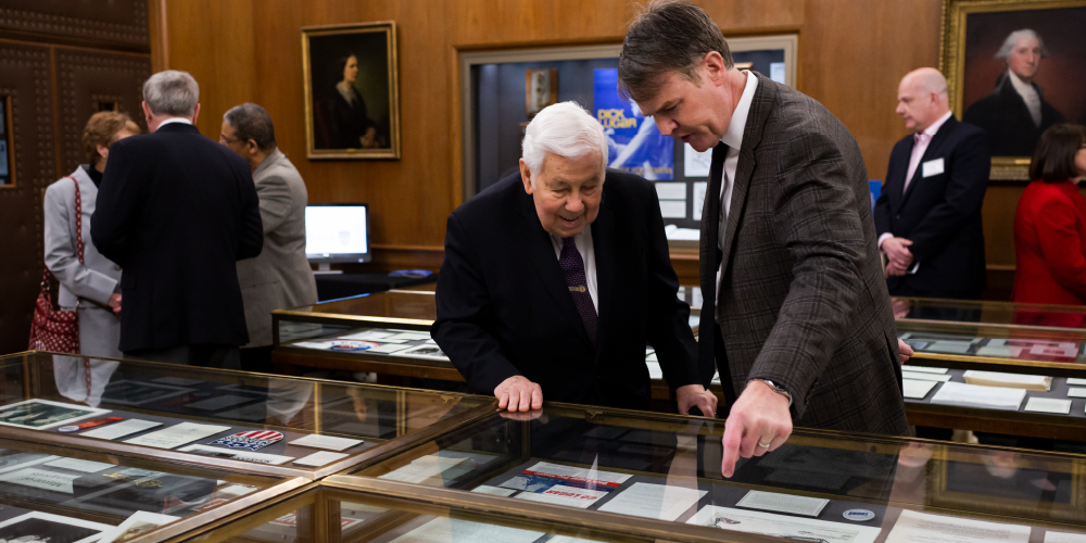 two men looking in a glass case at documents